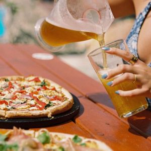 Woman pouring beer into glass at table with pizza in a Scarborough pizza place.